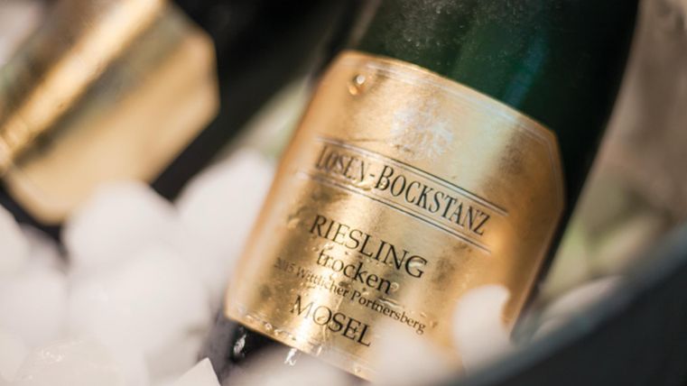 Twee flessen Rieslingwijn staan in een koeler met ijs. De etiketten tonen de naam van de wijn en de regio Mosel.