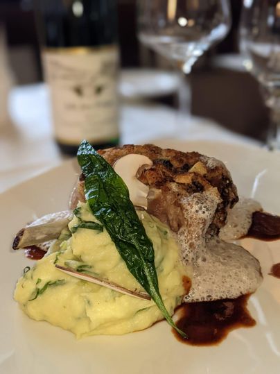 Ein köstliches Gericht mit gebratenem Fleisch, cremigem Kartoffelpüree und einer Soße. Dekoriert mit frischen Kräutern und einem Hauch von Schaum.