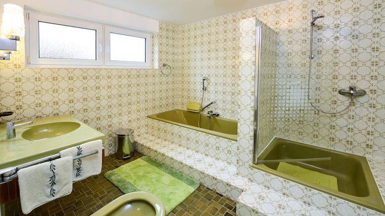 Ein Badezimmer mit einer Badewanne, einer Duschkabine und zwei Waschbecken. Die Wände sind mit auffälligen Fliesenmustern gestaltet.