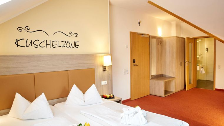 Een gezellige slaapkamer met een groot bed en witte kussens. De muren zijn licht van kleur en er is een aangrenzende ruimte met douche en toilet.