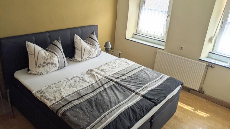 A cozy bedroom with a double bed and decorative pillows. A pleasant wooden floor and windows ensure plenty of daylight.