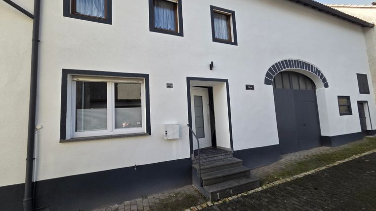 A modern residential building with a bright facade and large windows. The staircase leads to the entrance, next to it is a large driveway.