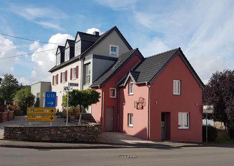A charming combination of two houses, one pink and one gray, at a street corner. The buildings are surrounded by trees and visible under a clear sky.