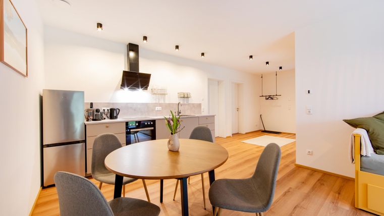 Eine moderne Küche mit einem runden Tisch und vier Stühlen. Der Raum hat helle Wände und einen eleganten Holzfußboden.