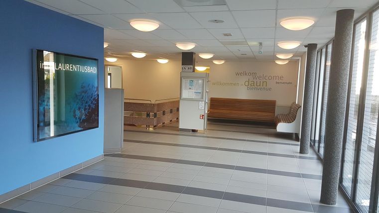 A bright reception area with modern furniture. A screen hangs on the wall displaying information.