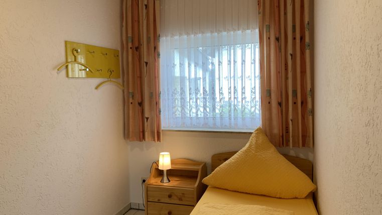 Ein gemütliches Schlafzimmer mit einem Einzelbett und einem Nachttisch. Das Fenster lässt viel Licht herein und die Vorhänge sind hell und freundlich.