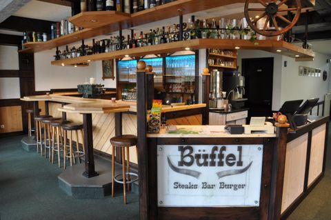 Ein modernes Restaurant mit einer Holzbar und einer großen Auswahl an Getränken. Die Einrichtung ist gemütlich und einladend.