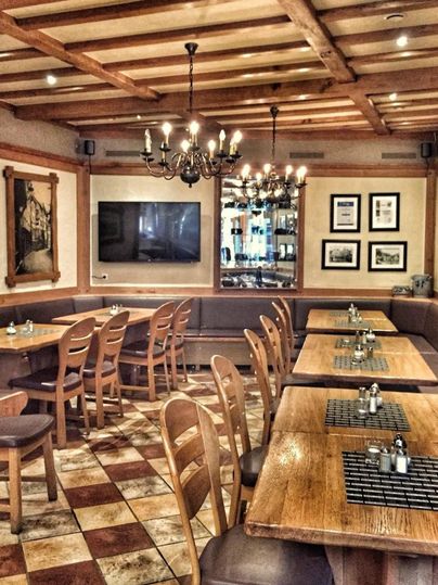 Ein gemütliches Restaurant mit Holzmöbeln und warmem Licht. Die Tische sind ordentlich gedeckt und die Wände sind mit Bildern dekoriert.