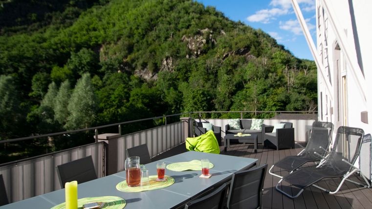 Ein schöner Balkon mit einem Tisch und Stühlen, umgeben von grünen Bergen. Auf dem Tisch stehen Getränke und eine entspannte Sitzgelegenheit lädt zum Verweilen ein.