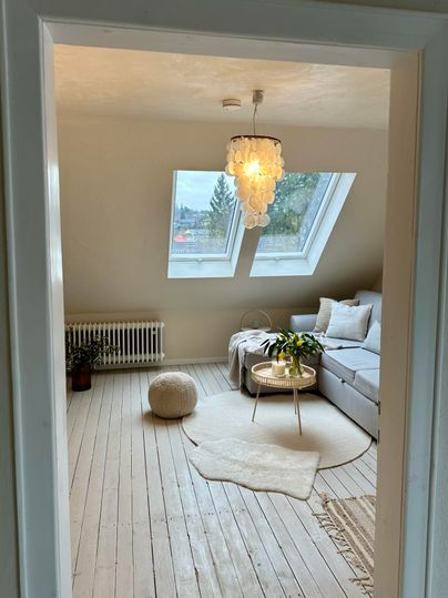 Een lichte woonkamer met grote ramen en een witte bank. De ruimte is modern en knus ingericht met een tapijt en een plant.