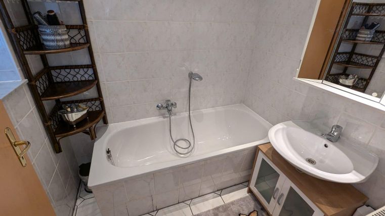 A bathroom with a bathtub and a sink. Shelves on the wall contain decorative elements.