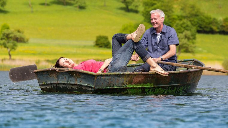 Eine entspannte Bootsfahrt auf einem ruhigen See. Zwei Personen genießen die Sonne und die Natur.