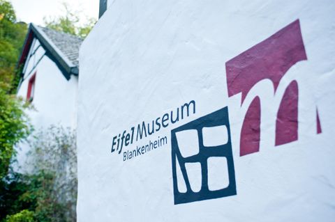 Een bord van het Eifel Museum in Blankenheim, dat de gevel van een gebouw siert. Het toont de naam van het museum en een modern logo.