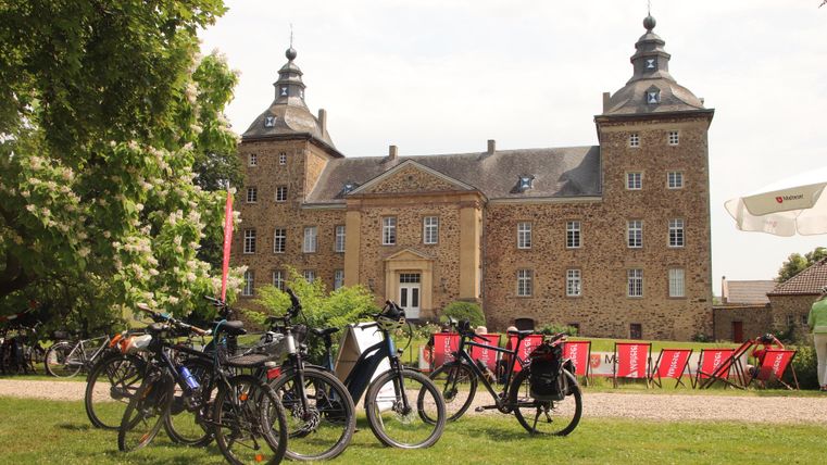 Een indrukwekkend kasteel met een mooie tuin. Op de voorgrond staan meerdere fietsen.