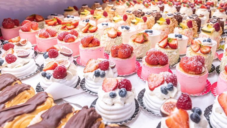 A colorful selection of small cakes and desserts, garnished with fresh fruits. The treats shine in various colors and invite you to try them.