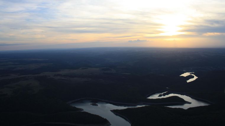 A beautiful view of a river winding through the landscape. The sun sets on the horizon and illuminates the sky.