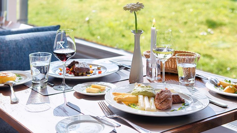 Elegante lunch met vlees, asperges, rode en witte wijn op een gedekte tafel bij het raam met uitzicht op het groen.