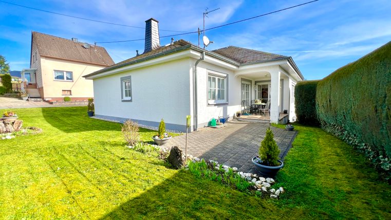 A modern, white house with a well-maintained garden. The green lawn and planting create an inviting atmosphere.