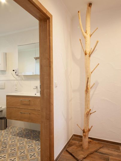 Ein heller Raum mit einem Holzrahmen und einem modernen Badezimmer. In der Ecke steht ein dekorativer Baumstamm.