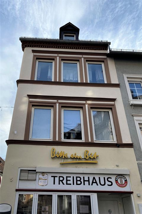 Ein mehrstöckiges Gebäude mit grauer Fassade und gelbem Schriftzug „bar am See“. Im Erdgeschoss befindet sich das Restaurant „TREIBHAUS“.