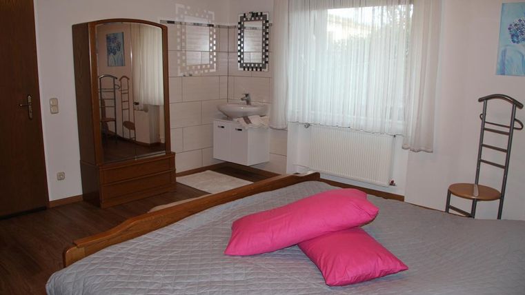 A cozy bedroom with a large bed and pink pillows. The room has a window and a makeup mirror.