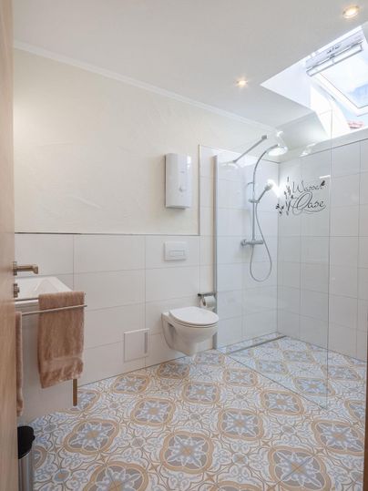 Ein modernes Badezimmer mit einer Dusche und einem weißen WC. Der Boden hat ein stilvolles, gemustertes Fliesendesign.