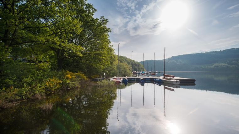 A quiet lake surrounded by trees and a boat dock. The sun shines brightly over the water and reflects in it.