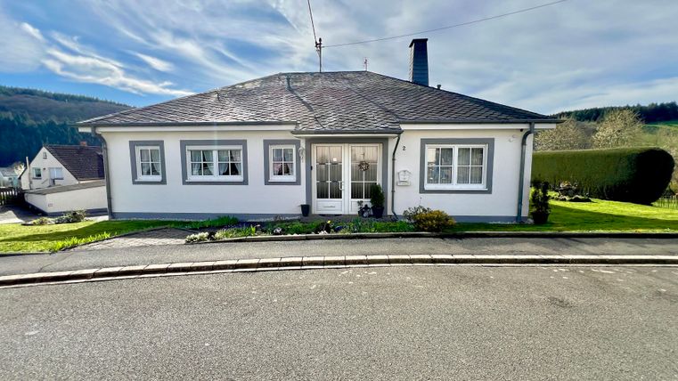 A modern single-family house with a flat roof. It is located in a quiet area with green spaces in the foreground.