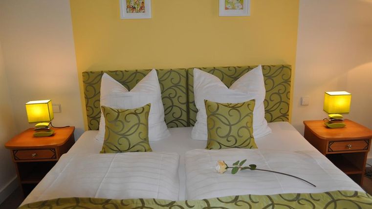 Ein gemütliches Schlafzimmer mit einem großen Bett und dekorativen Kissen. Neben dem Bett stehen zwei Nachttische mit warmen Lampen.