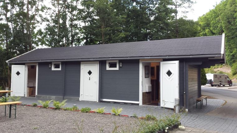 Ein modernes Gebäude mit grauer Fassade und mehreren Eingängen. Es befindet sich in einer ruhigen Umgebung mit Bäumen im Hintergrund.