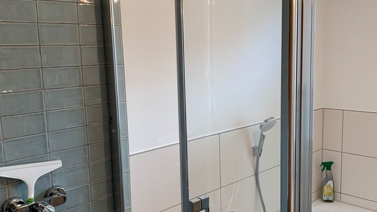 Een moderne badkamer met een douche en een bad. De muren zijn licht betegeld en er staan verschillende verzorgingsproducten op de rand.