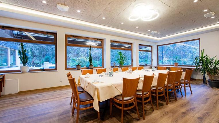 Ein eleganter Restaurantbereich mit einem großen Tisch und Holzstühlen. Große Fenster bieten einen Blick auf die Grünfläche draußen.