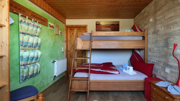 A cozy room with a bunk bed and a single bed. The walls are painted in vibrant colors and there are simple wooden furniture.