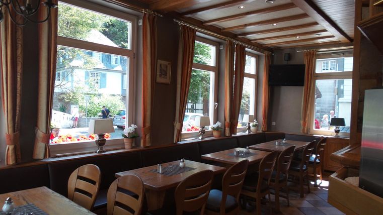 Ein einladendes Restaurant mit Holztischen und Stühlen. Große Fenster sorgen für viel natürliches Licht und einen Blick nach draußen.