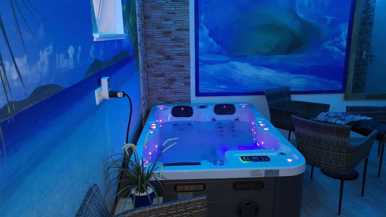Ein entspannender Whirlpool in einem modernen Raum mit blauen LED-Lichtern. Eine malerische Wandmalerei zeigt eine Küstenlandschaft.