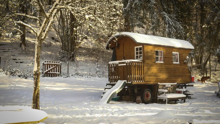 Een gezellig houten huis in de sneeuw, omgeven door bomen. De tuin is bedekt met verse sneeuw en er is een kleine glijbaan.