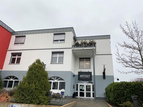 Ein modernes Gebäude mit dem Schriftzug "ARTIST" an der Fassade. Vor dem Gebäude stehen einige Bäume und Sträucher.