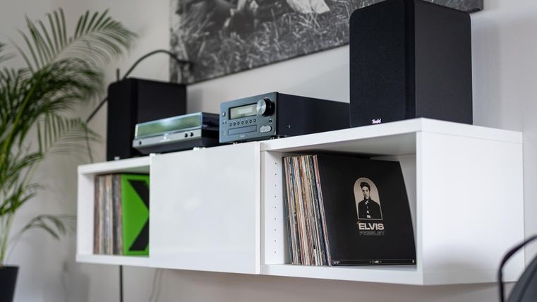 Ein moderner Regal mit zwei Lautsprechern und einem Plattenspieler. Darunter liegen verschiedene Schallplatten, darunter eine von Elvis.