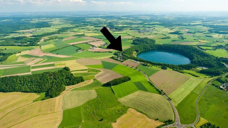 Een uitgestrekt, groen landschap met velden en bossen. Op de achtergrond bevindt zich een heldere vijver.