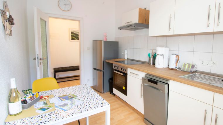 Eine moderne Küche mit hellen Wänden und einem Holzarbeitsbereich. Der Raum ist gut ausgestattet mit einem Herd, Kühlschrank und einem kleinen Essbereich.