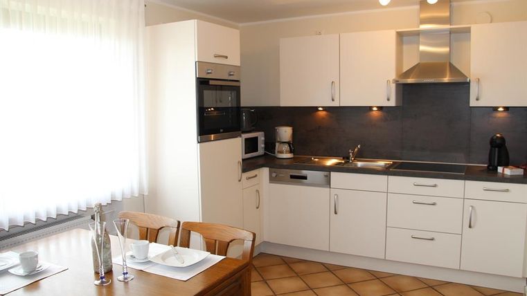 A modern kitchen with white cabinets and a dark countertop. The dining area consists of a wooden table and chairs.