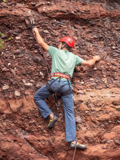 Een klimmer met een helm klimt tegen een rotswand. Hij draagt klimuitrusting en concentreert zich op de volgende greep.