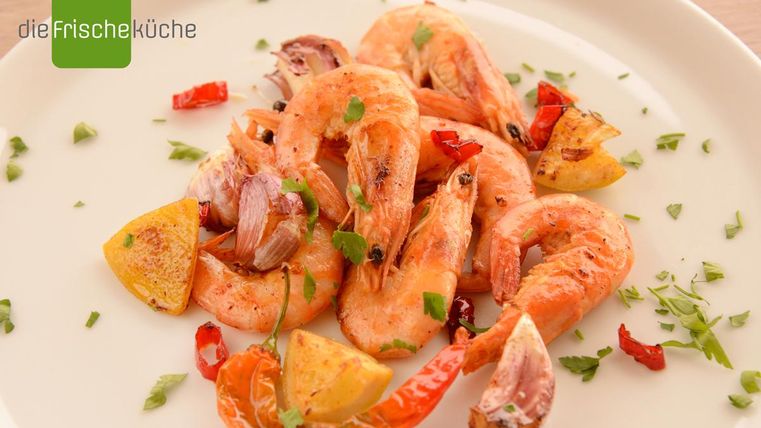 Ein Teller mit gebratenen Garnelen, garniert mit roten Paprikastreifen und Zitronenscheiben. Frische Kräuter verleihen dem Gericht zusätzlichen Geschmack.