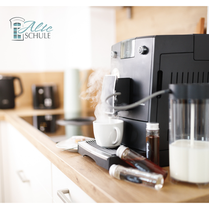 Eine moderne Kaffeemaschine steht auf der Küchenzeile und dampft. Eine Tasse Kaffee wird vorbereitet, während verschiedene Zutaten daneben liegen.