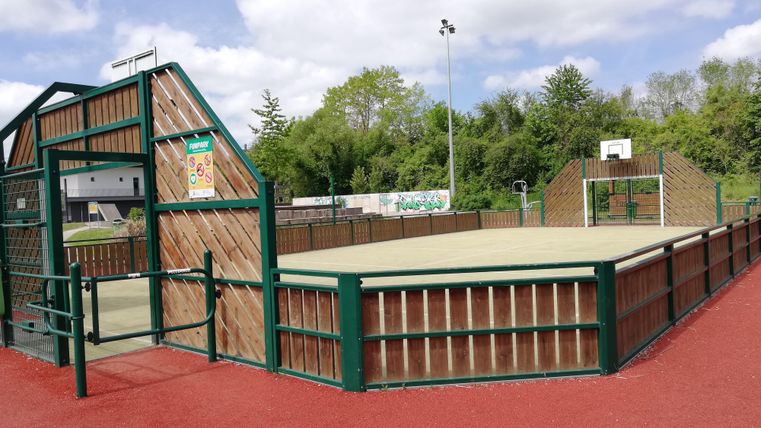 Een sportveld met een omheind gebied voor basketbal en andere spelletjes. De omgeving is groen en uitnodigend.