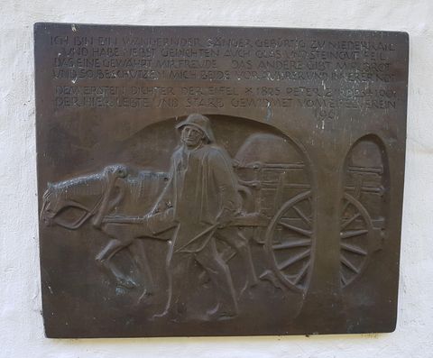 A bronze plaque depicting a man pulling a horse-drawn cart. Above are engravings of text inscriptions.