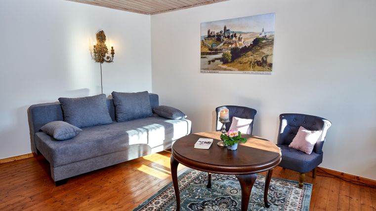 An elegantly furnished living space with a blue sofa and two chairs. A round table stands in the middle, while a picture on the wall adds a decorative touch.