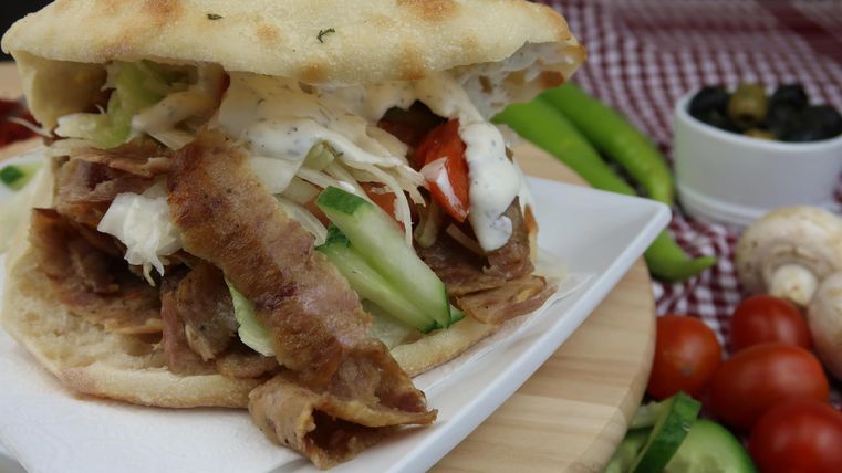 Ein frisch zubereitetes Sandwich mit Fleisch, Salat und Gemüse in einem Brot. Im Hintergrund sind verschiedene frische Zutaten zu sehen.