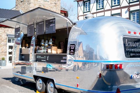 Ein glänzender Food-Truck im Vintage-Stil steht auf einem Platz. Er bietet eine einladende Auswahl an Speisen und Getränken an.