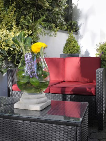 Ein gemütlicher Außenbereich mit rot gepolsterten Möbeln und einem Tisch aus Rattan. Auf dem Tisch steht eine dekorative Blumenvase mit bunten Blumen.